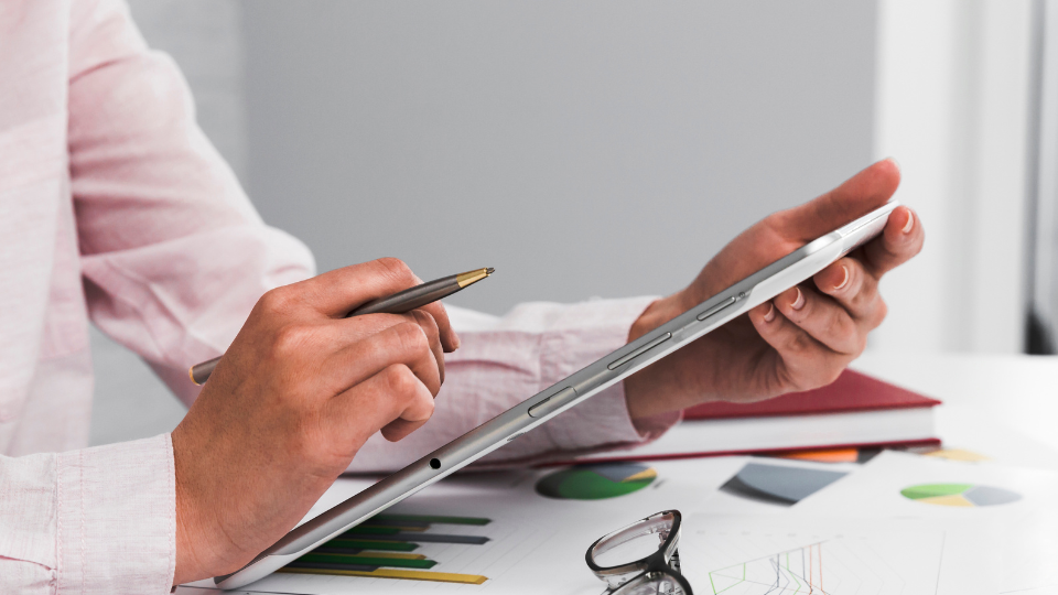 A person conducts an income assessment on a tablet with financial documents on the desk