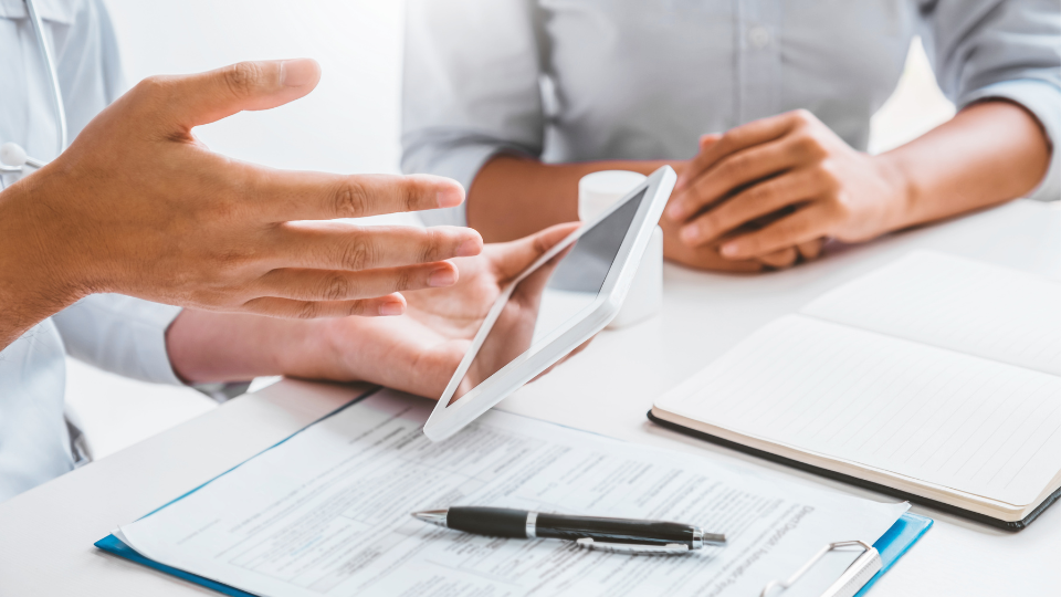 Two people review agency guidelines on a tablet before signing a form on the table