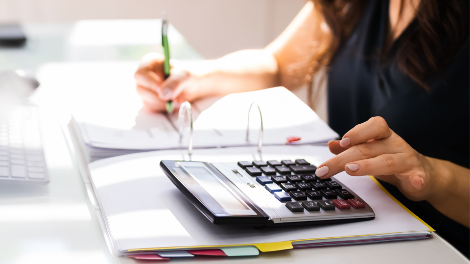 A person sitting at a desk uses a calculator and income documents to calculate variable income