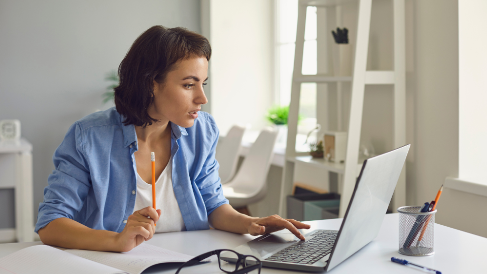 A freelancer works on a laptop at a desk with a pencil in hand