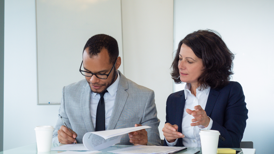 A mortgage underwriter reviews mortgage loan documents for errors with a potential borrower at their desk