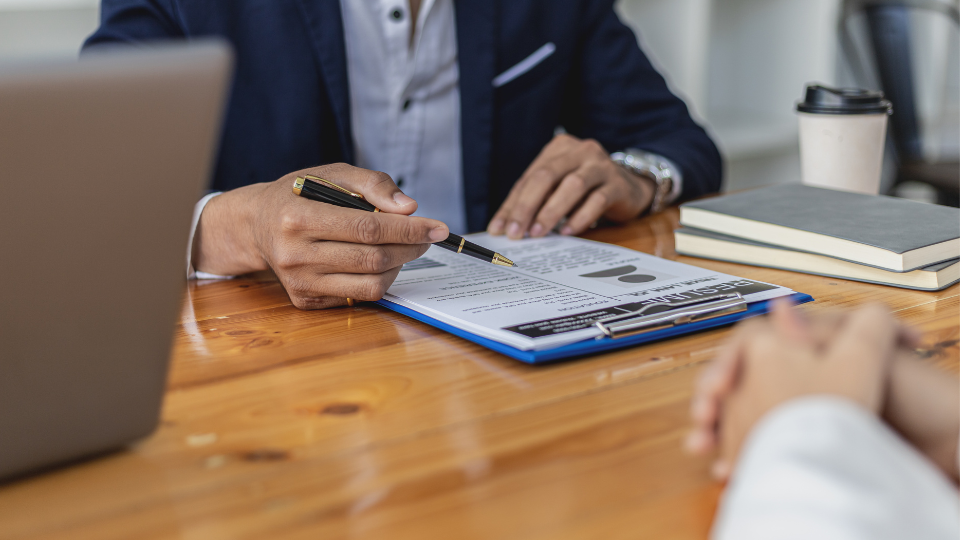 A lender sits with two borrowers and reviews their mortgage options on a clipboard