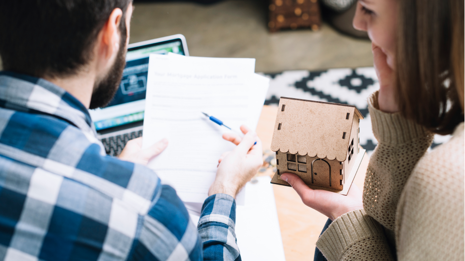 A couple reviews FHA compensating factor documents while holding small model house