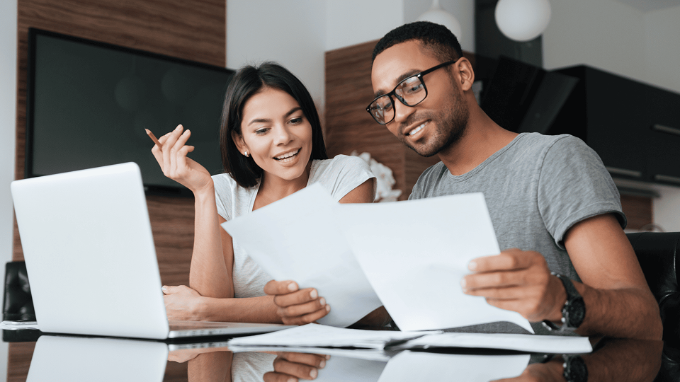 A man and woman sit at a table and review mortgage documents in front of a laptop