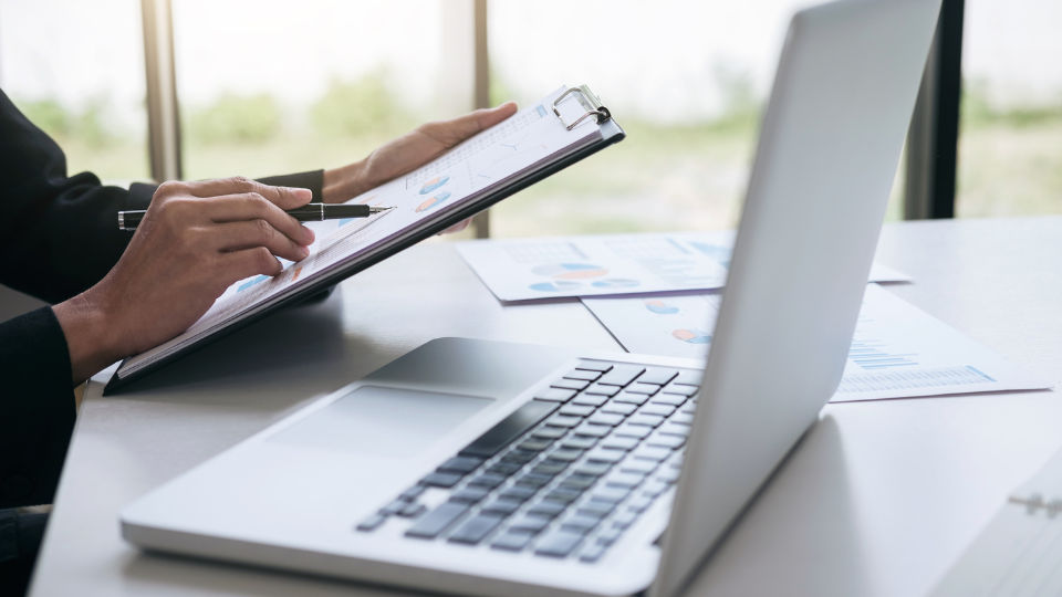 A lender reviews documents on a clipboard next to a laptop