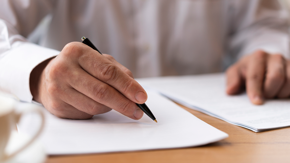 A close-up of a person holding a pen and reviewing loans on a desk